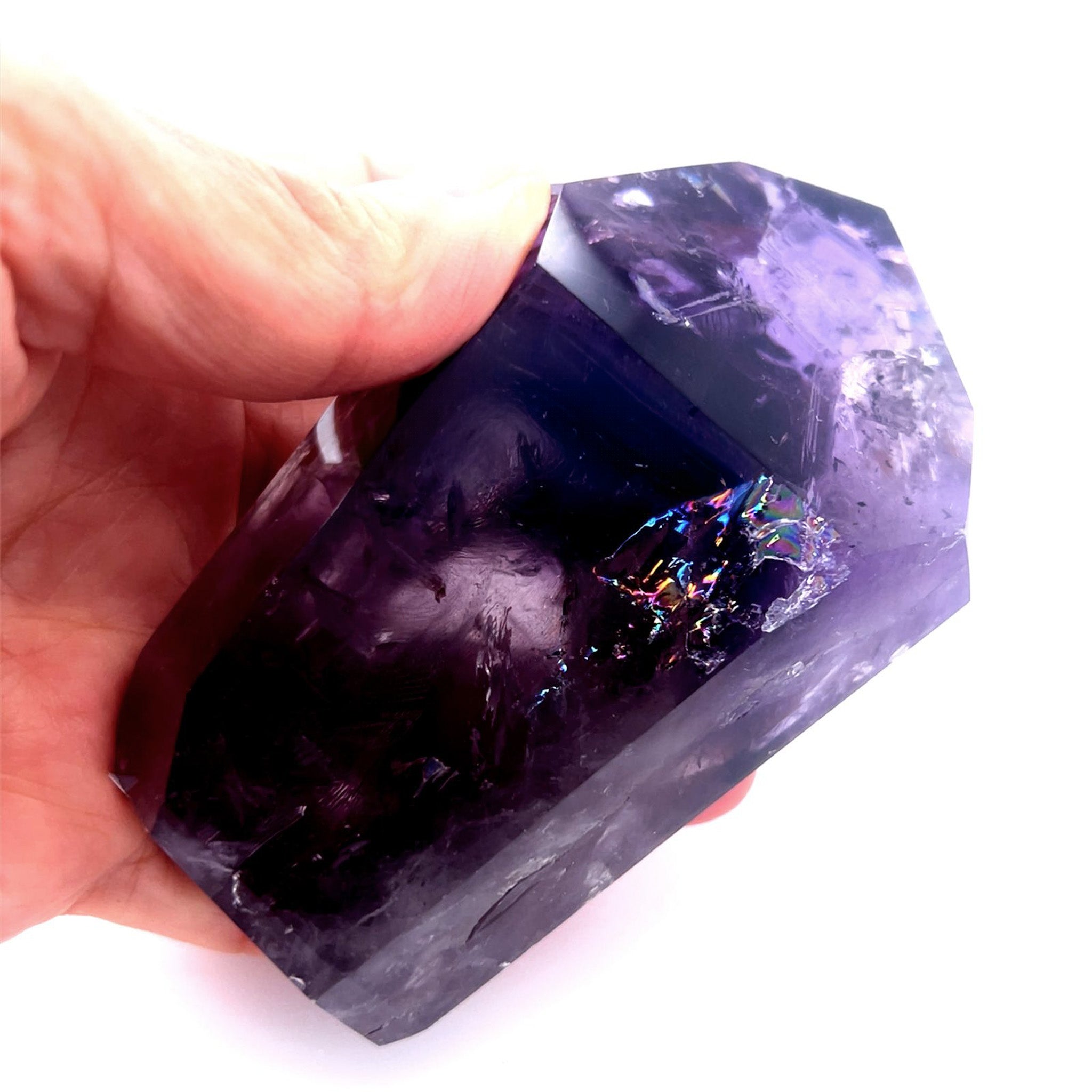 A hand holding a large, polished purple amethyst crystal with natural inclusions and a small iridescent rainbow inlay, set against a solid white background.
