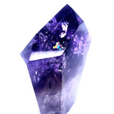 A natural purple amethyst crystal point with visible internal inclusions and sparkling rainbows, photographed against a solid white background.
