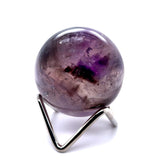 A polished purple amethyst crystal sphere resting on a silver metal display stand, isolated on a white background.