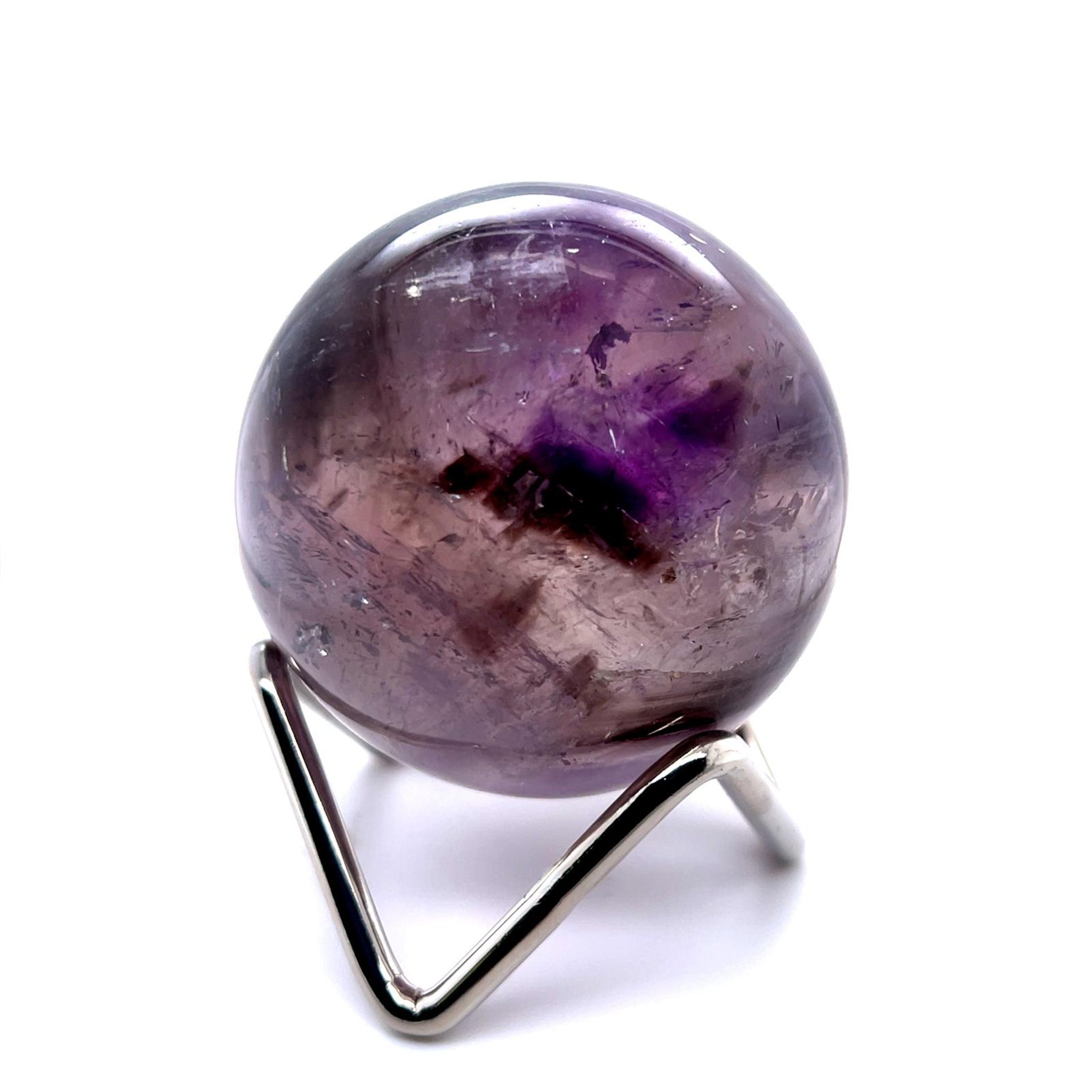 A polished purple amethyst crystal sphere resting on a silver metal display stand, isolated on a white background.